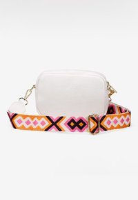 Bolso de cuero blanco cruzado con una correa de tela estampada en diseños geométricos en rosa, naranja y negro. Presenta acentos de hardware dorado.