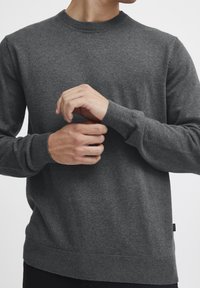 Suéter de punto gris con cuello redondo, puños y dobladillo acanalados, textura suave y corte ajustado. Detallado con una marca mínima en el dobladillo.