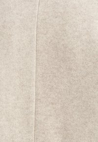 Tessuto in feltro beige con una consistenza morbida, caratterizzato da un motivo sottile e un dettaglio di cucitura verticale. Adatto per indumenti o accessori.