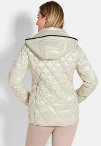 Helle beige, gesteppte Pufferjacke mit Kapuze, die durch eine glänzende Oberfläche und schwarze Akzente am Kragen besticht. Das Design umfasst ein Rautenmuster.