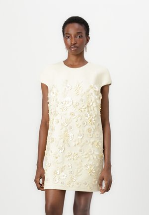 Robe à manches courtes, couleur crème, en tissu texturé, ornée de broderies florales élaborées en blanc et accents dorés sur le devant.