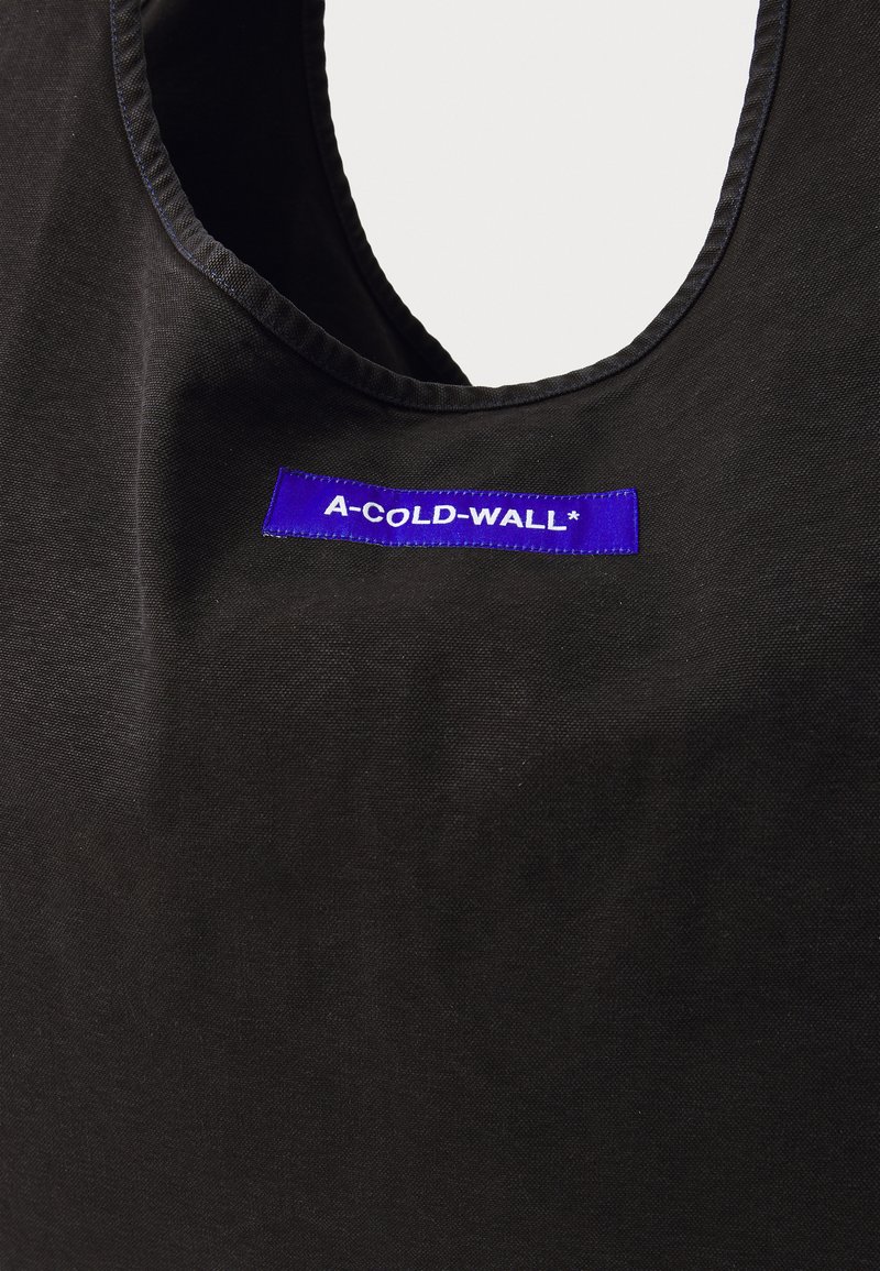 Czarna torba na ramię z płótna z okrągłym otworem, fioletową metką z napisem "A-COLD-WALL*" wyszytym na niej oraz gładką, matową fakturą.