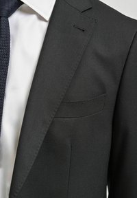 Grå kavaj med en texturerad svart slips, vit skjorta och en diskret näsduk. Skräddarsydd passform och eleganta knappdetaljer.