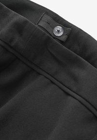Schwarze Hose aus glattem, strukturiertem Stoff. Der Bund verfügt über einen Knopf und eine Schlaufe zur Anpassung. Keine sichtbaren Muster.