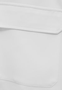 Weißer Stoff mit glatter Textur, ausgestattet mit einer auffälligen Tasche, klaren Nähten und einem flachen Design, minimalistisch im Stil.