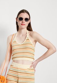 Top cropped de malha em halter com riscas horizontais em laranja, verde e creme. Combinado com calças listradas a condizer e uma pequena mala laranja.