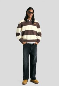 Barna és krém csíkos pulóver gallérral, fekete farmernadrág és homokszínű csizma. Kiegészítők között sötét napszemüveg is szerepel. Laza, kényelmes fazon.