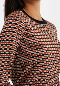 Monivärinen neulepaita, jossa on aaltoileva kuvio oranssin, mustan ja kerman sävyissä. Klassinen pyöreä kaula-aukko ja resorireunaiset hihansuut. Pehmeä tekstuuri.