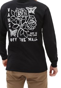 Musta pitkähihainen paita, jossa on valkoinen graafinen kuvasto, joka sisältää ruusuja, perhosia ja tekstit "VANS OFF THE WALL" ja "NOW IS THE TIME."