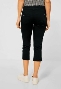 Pantaloni capri in jeans neri con un design aderente, vita medio-alta e tasche posteriori cucite, abbinati a sneakers bianche con piattaforma.