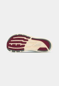 Shoe outsole featuring a textured design in cream, burgundy, and green, with distinct grooves and a logo detail for traction.