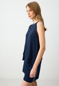 Marineblauw mouwloos topje met een gelaagd ontwerp, gladde textuur en ronde halslijn. Gecombineerd met bijpassende shorts met zijkanten in een streepdesign.