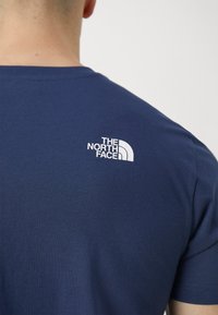 Navy blue cotton t-shirt with short sleeves, featuring a white logo on the upper back that reads "THE NORTH FACE." Smooth texture.