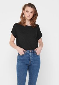 Svart t-skjorte med korte ermer og løs passform, kombinert med høyt liv blå jeans. T-skjorten har rullede ermer.