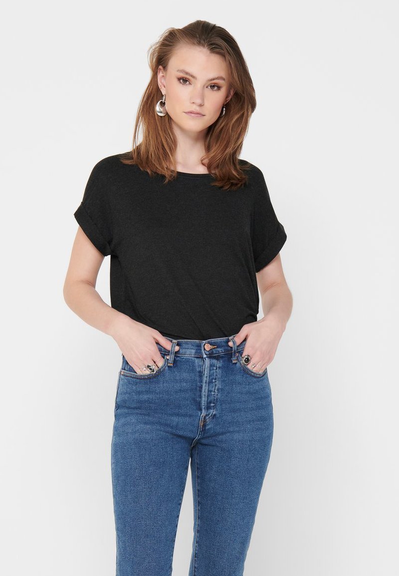 Svart t-skjorte med korte ermer og løs passform, kombinert med høyt liv blå jeans. T-skjorten har rullede ermer.