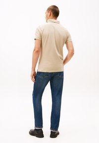 Béžové polo tričko s krátkými rukávy, doplněné modrými džínami a černými botami. Tričko má límec a jemné detaily šití.