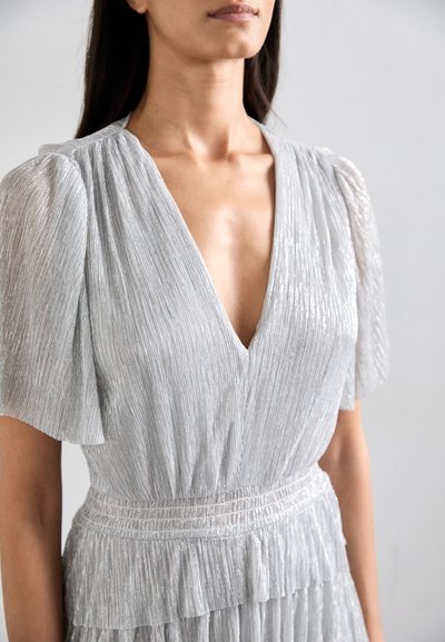 Silver pleated dress with a deep V-neck, short puff sleeves, and a ruffled hem, featuring a textured, shimmering fabric.