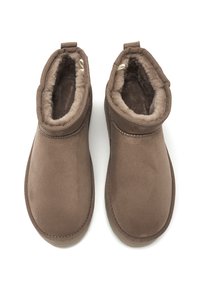 Botas marrones, de material similar al ante, con un forro suave y peludo. Forma redondeada, diseño de tobillo bajo y un simple acento de costura alrededor del cuello.