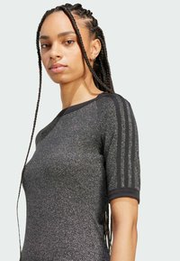 Czarny sportowy top z krótkim rękawem, o błyszczącej teksturze i trzema czarnymi paskami na ramionach. Dopasowany krój.