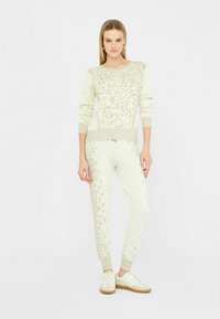 Set di maglia e pantaloni color crema con una sottile stampa leopardata, polsini a coste e una vestibilità rilassata, abbinato a sneakers chiare.