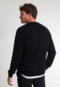 Maglione nero in morbido tessuto a maglia con collo rotondo, maniche lunghe e polsini a coste. Texture liscia senza motivi visibili.