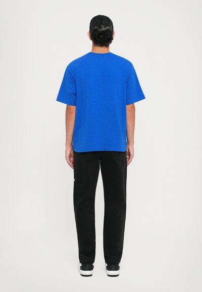 Blå bomulls t-skjorte med korte ermer og rett snitt, kombinert med svarte jeans. Bakgrunnen er helt hvit for kontrast.