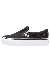 Scarpe sneaker slip-on nere Vans con suola bianca, cuciture bianche e piccolo tag con il logo Vans sul lato, su sfondo bianco.