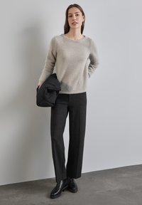 Pullover grigio chiaro, strutturato, con maniche lunghe, abbinato a pantaloni neri a gamba larga. Una giacca a vento nera è appoggiata sul braccio.