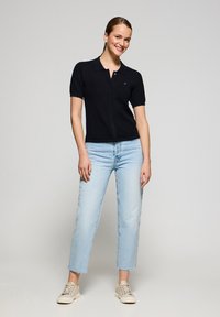 Polo shirt navale a trama con maniche corte, patta con bottoni e logo sul lato sinistro del petto, abbinato a jeans azzurri a gamba dritta e sneakers nei toni neutri.