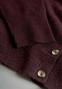 Ciemnobordowy kardigan o prążkowanej teksturze, z dwiema okrągłymi, kontrastującymi guzikami z przodu. Miękki materiał wełniany z widocznymi włóknami.