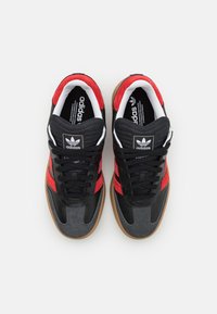 Svarta och röda sportskor med överdel i mocka och läder, med gummisula, strukturerade detaljer och logotyp på tungan.