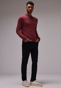 Pull en maille bordeaux avec un col montant, des poignets et un ourlet côtelés ; associé à un jean noir et des baskets blanches avec des accents beige.