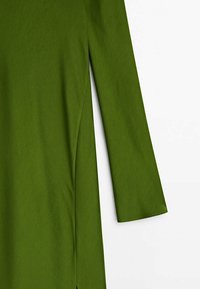 Manche droite et fente latérale d'une robe verte à manches longues sur fond blanc.