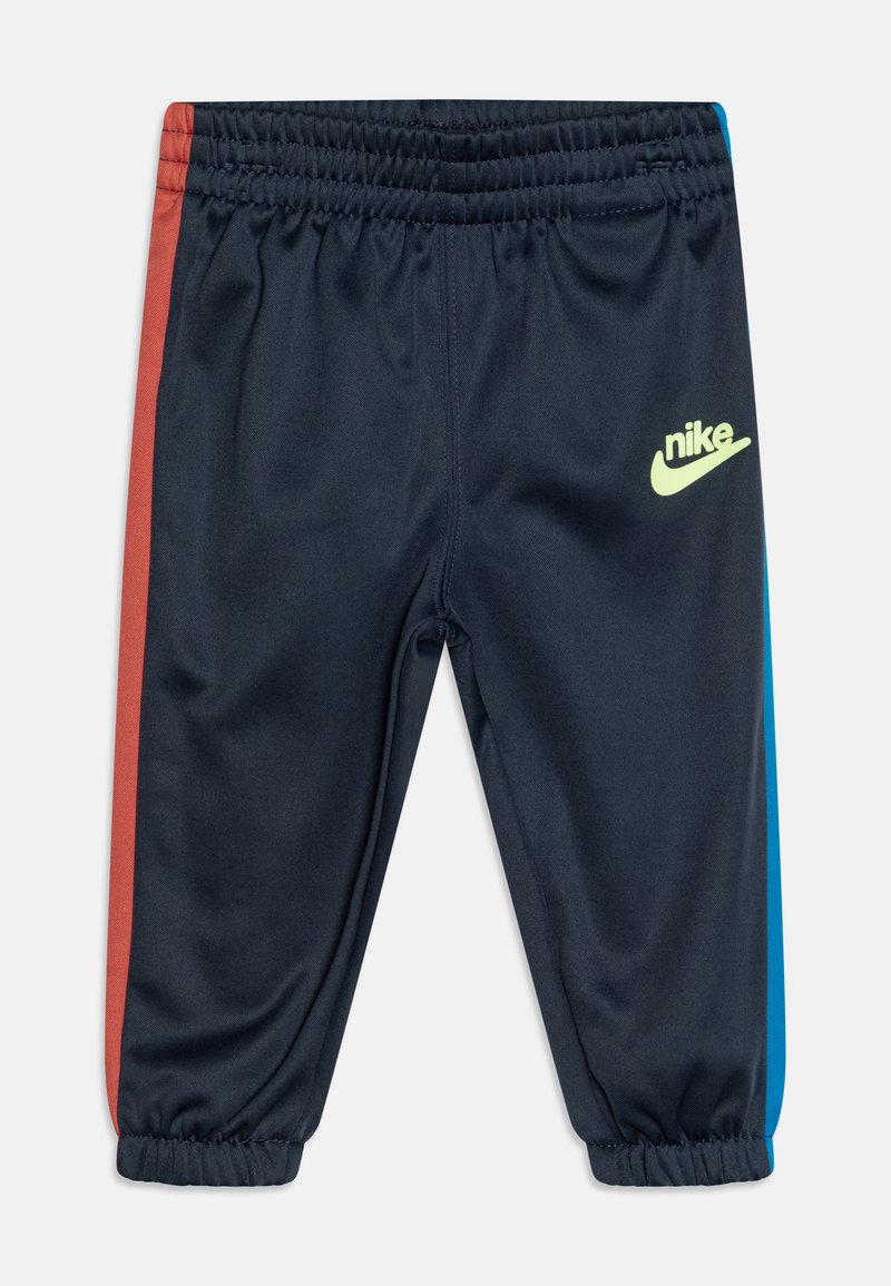 Pantalones deportivos de color navy con rayas laterales rojas y azules, cinturilla elástica y un logo de Nike en color verde lima en el lado derecho. Textura de tela suave.