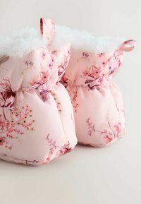 Bottines florales roses avec un design rembourré et une douce doublure en fausse fourrure blanche. Présente des fronces élastiques et de petites boucles pour une manipulation facile.
