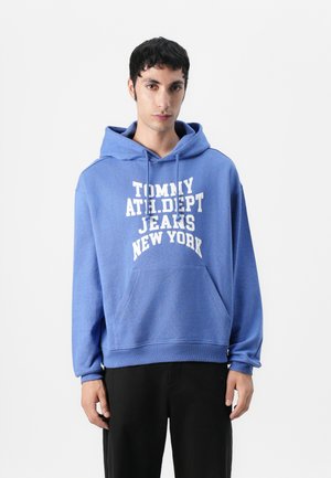 Blue hoodie made of cotton with a front kangaroo pocket. Features white text “TOMMY ATH. DEPT. JEANS NEW YORK” across the chest.