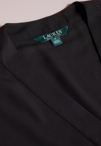 Svart tyg med en "Lauren Ralph Lauren" klädesetikett sydd inuti halsringningen, som visar storlek och tillverkningsdetaljer.