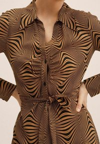 Robe-chemise à motif marron et noir, dotée d'un col, d'une fermeture à boutons, de manches longues et d'une ceinture à la taille.