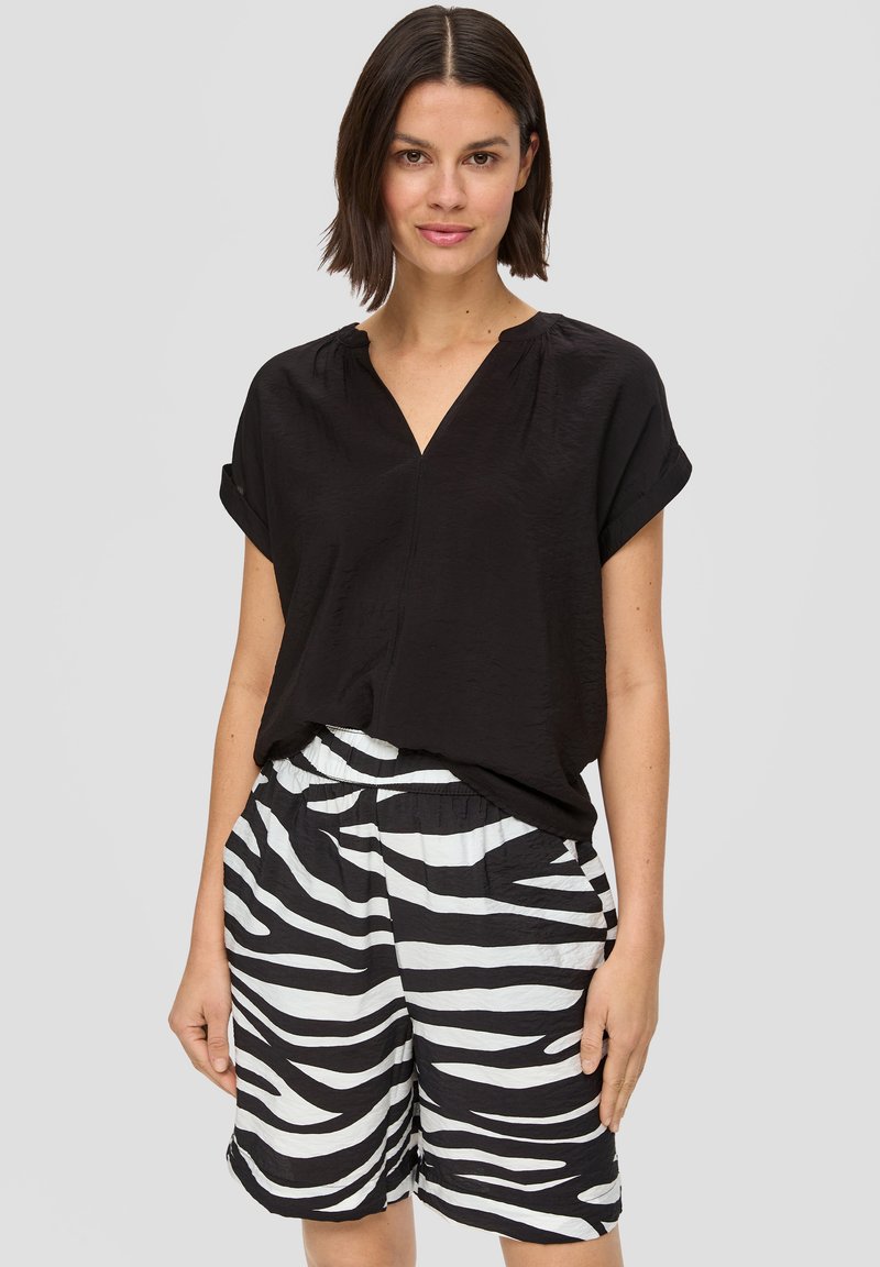 Czarna bluzka na krótki rękaw z dekoltem w serek, w połączeniu z białymi i czarnymi spodniami w paski, posiadającymi elastyczny pas i boczne kieszenie.