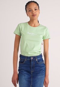 Vaaleanvihreä, lyhythihainen t-paita, jossa on vartalonmyötäinen muotoilu ja valkoinen "Pepe Jeans" -logo. Yhdistetty siniseen farkkuhameeseen, jossa on ompelut yksityiskohtia.