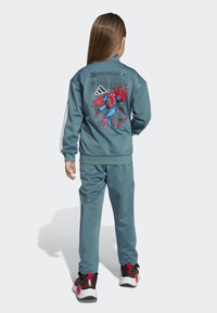 Teal-jumpsuit, jossa on Spiderman-kuva takana, valkoiset raidat hihoissa ja mustat-punaiset kengät, joissa on ainutlaatuisia korostuksia.