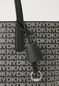 Μαύρη τσάντα tote με ανάγλυφο μοτίβο λογότυπου, λείες δερμάτινες λεπτομέρειες και ετικέτα στερεωμένη με ασημένιο δαχτυλίδι. Υφασμάτινη επιφάνεια.