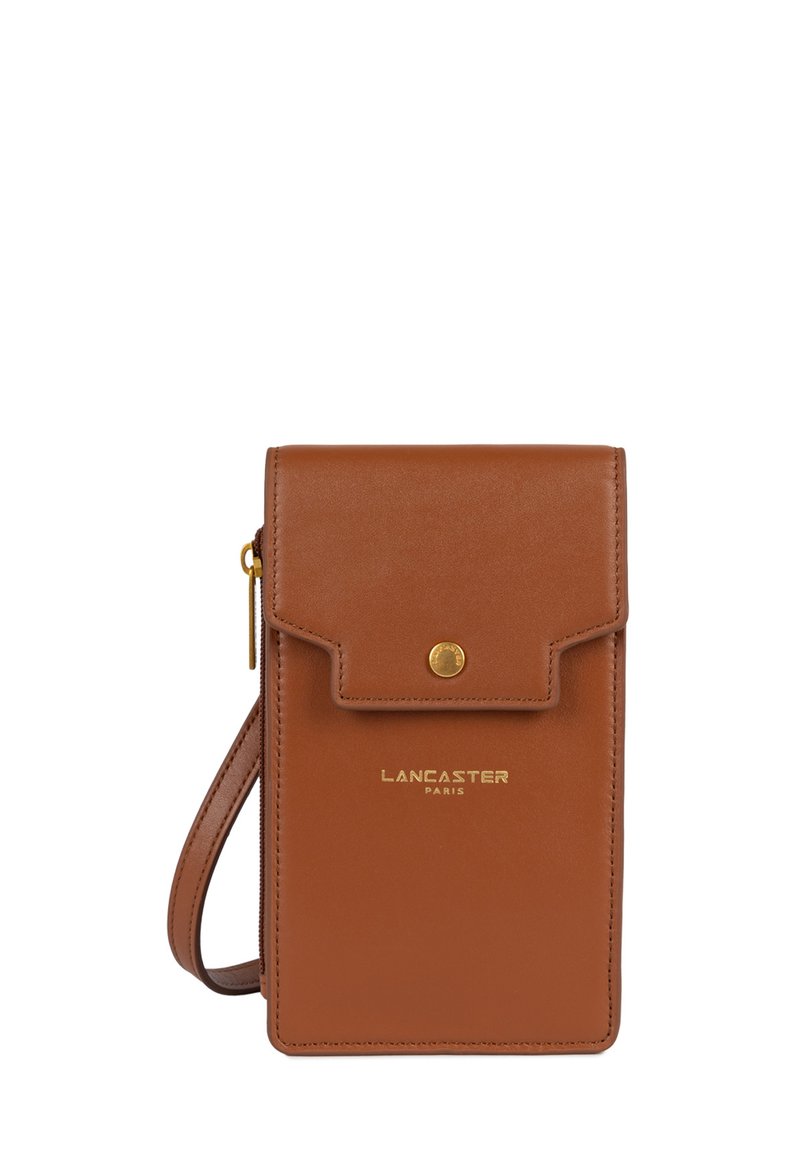 Bruine leren tas met een klep en gouden hardware. Kenmerken zijn een logo aan de voorkant, een verstelbare schouderband en een gladde textuur.