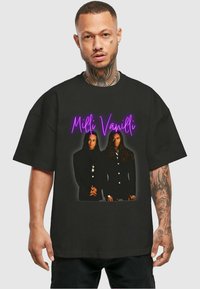 Must see must have must be cool t-särk, millel on graafiline print kahest ülikonnaga inimesest, nende kohal neoonroosa tekstiga "Milli Vanilli".