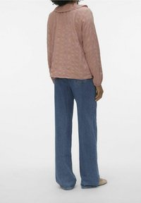 Blouse longue à manches longues rose clair texturée avec un grand col, associée à un jean bleu à jambes larges, vue de dos.