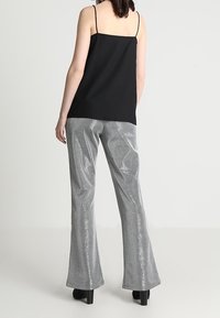 Camisole noire à fines bretelles associée à un pantalon évasé argenté brillant, présentant une texture lisse et un léger éclat. Des talons noirs sont portés.