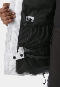 Interior de chaqueta blanca y negra con un forro de malla estampada, ajuste con cordón y botones a presión en los bordes.