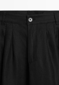 Pantaloni neri di lino con chiusura a bottone, passanti per cintura e pieghe frontali.