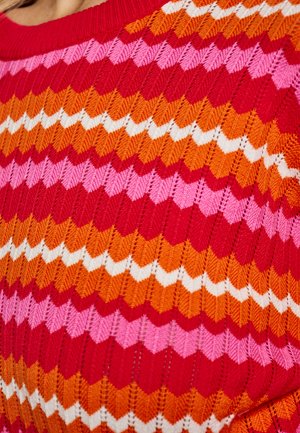 Pletený svetr s vzorem chevron v červené, růžové, oranžové a bílé barvě. Textura je hladká s žebrovaným výstřihem a živými barvami.