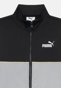 PUMA zip-up jack in het zwart en grijs, met een hoge kraag, ritssluiting en gele accentlijn. Zachte stof met logo-detail op de borst.